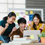 Group of Asia young creative people in smart casual wear discussing business celebrate giving five after dealing feeling happy and signing contract or agreement in office. Coworker teamwork concept.